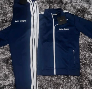 Blå träningsjacka från Palm Angels - Snygg blå dress från Palm Angels med vita detaljer och dragkedja. Jackan har långa ärmar och en sportig look med vit text på bröstet. Perfekt för en avslappnad stil.