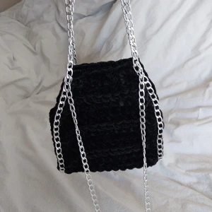 Svart virkad väska med kedjor - Snygg svart virkad väska med silverfärgade kedjor. Perfekt för att ge din outfit en edgy touch. Väskan har en unik textur och är både stilren och praktisk.