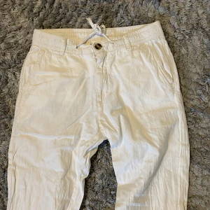 Linnebyxor från Lindbergh - Snygga vita byxor från Lindbergh med snörning i midjan och knappstängning. Perfekta för en stilren look. Byxorna har en avslappnad passform och är tillverkade i ett lätt material som passar bra för varmare väder.