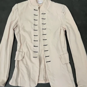 Kavaj  - Säljer en stilren ljusrosa jacka från Chica London med svarta knytningar fram. Jackan har en modern design med långa ärmar och två fickor, har också puffar vid axlarna som gör att jackan har en bättre form. (Syns ej att den är rosa i kamera) 🩷