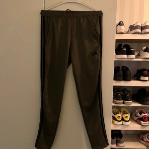 Gröna träningsbyxor från Adidas - Snygga gröna träningsbyxor från Adidas med svarta detaljer längs sidorna. Byxorna har en elastisk midja och dragsko för justerbar passform. Perfekta för träning eller en avslappnad dag. Byxorna är i storlek S. Byxorna är i mycket bra skick 