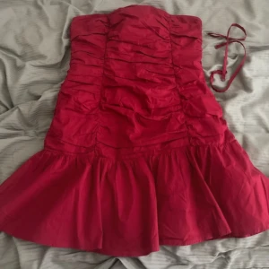 Röd axelbandslös klänning från Gina Tricot - Säljer en snygg röd axelbandslös klänning från Gina Tricot. Klänningen har en volangdetalj vid fållen och en smickrande rynkad design. Perfekt för en kväll ute eller en speciell tillställning. 💃