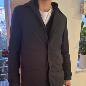 Svart rock från Aspesi - Snygg svart rock från Aspesi med en stilren design. Nypris cirka 500 euro. Rocken har långa ärmar och knäppning framtill. Insidan har en cool orange detalj som ger en extra touch. Den är köpt förra året.