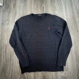 Mörkblå stickad tröja från Ralph Lauren - Säljer en snygg mörkblå stickad tröja från Ralph Lauren med kabelstickat mönster. Tröjan har en broderad röd logga på bröstet och långa ärmar. Perfekt för kyliga dagar! Det står att den är i XL men är i barn storlek, den passar S dock