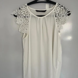Vit blus från Zara Basic Small -  elegant vit blus från Zara Basic med vackra spetsdetaljer på axlarna. Blusen har en lös passform. Storlek Small.