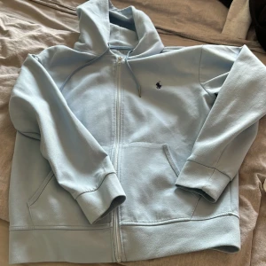 Ljusblå hoodie från Ralph Lauren - Säljer en stilren ljusblå hoodie från Ralph Lauren med dragkedja och klassisk logga på bröstet. Perfekt för en avslappnad stil. Den har en bekväm passform och är tillverkad i mjukt material. Hör av dig vid intresse! 💙