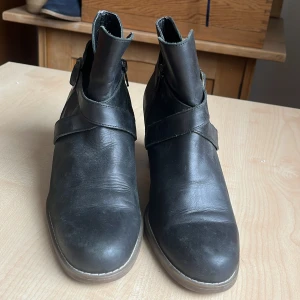 Svarta boots med klack från Björn Borg  - Snygga svarta boots i skinn med klack och spänndetalj från Björn Borg . Perfekta för en stilren look. De har en robust sula och en bekväm passform.