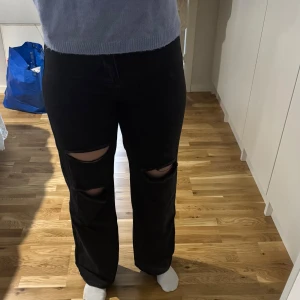 Svarta jeans med slitningar - Snygga svarta jeans med slitningar på knäna. De har en hög midja och en straight passform som ger en avslappnad look. Perfekta för en trendig stil.