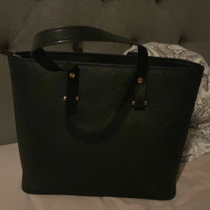 Svart axelväska med dragkedja - Snygg och stilren svart axelväska med praktisk dragkedja. Perfekt för att bära med sig det nödvändigaste. Väskan har en enkel design med två handtag och guldiga detaljer.