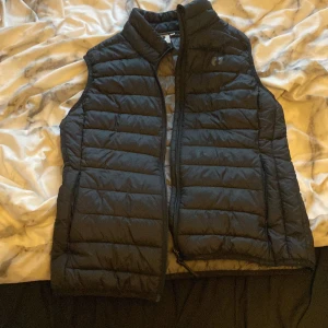 Svart dunväst från Hang Ten - Snygg svart dunväst från Hang Ten med dragkedja framtill. Perfekt för lager-på-lager under kyligare dagar. Västen har en stilren design med quiltade paneler.