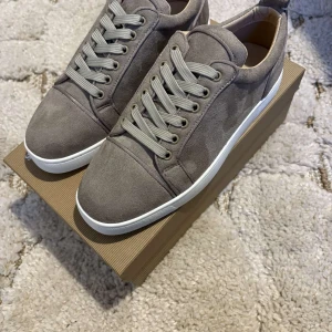 Grå sneakers från Christian Louboutin - Snygga grå sneakers från Christian Louboutin i mocka med den ikoniska röda sulan. Skorna har snörning och en vit sula som ger en stilren look. Perfekta för dig som vill ha en touch av lyx i vardagen.Inget kvitto därför har vi detta låga pris för vi kan ej garantera att den är äkta