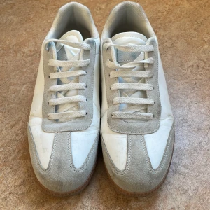 Vita och grå sneakers med mockadetaljer - Snygga vita sneakers med grå mockadetaljer och snörning. Skorna har en rund tå och en brun sula med bra grepp. Perfekta för en stilren och avslappnad look. Tvättas innan frakt