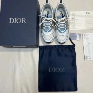 Dior b22 sky blue  -  Säljer ett par Snygga Dior b22 sky blue  en fräsch kombination av blått och vitt. Skorna har en modern design med snörning och rund tå. Perfekta för att ge din outfit en lyxig touch. Levereras med originalförpackning och dustbag skriv bara kan gå ner i pris 
