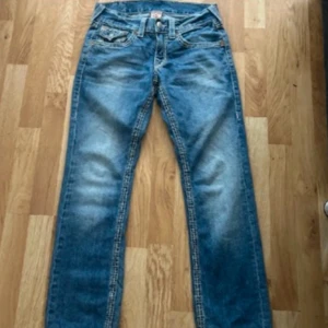 Blå jeans från True Religion - Snygga blå jeans från True Religion med klassisk femficksdesign och kontrastsömmar. Jeansen har en rak passform och är tillverkade i USA av mexikanskt tyg. Perfekta för en avslappnad stil.