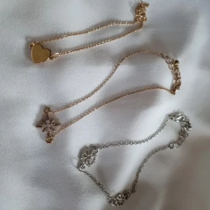 Tre armband med hjärta, stjärna och snöflinga - Säljer tre eleganta armband. Ett guldarmband med ett hjärta, ett guldarmband med en stjärna dekorerad med små stenar, och ett silverarmband med små snöflingor. Perfekta för att lägga till en touch av stil till din outfit. De kostar 15 kr styck, men 45 kr för alla 3.