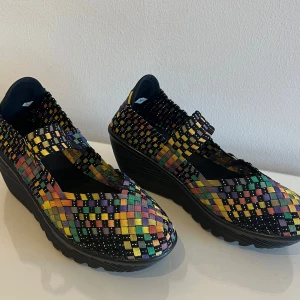 Flerfärgade flätade skor med kilklack - Unika flätade skor i regnbågens alla färger med en bekväm kilklack. Skorna har en elastisk rem över foten för extra stöd och en rund tå. Storlek 36