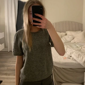 Grå stickad tröja - Säljer en stilren grå stickad tröja med korta ärmar. Perfekt för en avslappnad look. Tröjan har en rund halsringning och är i ett mjukt material.