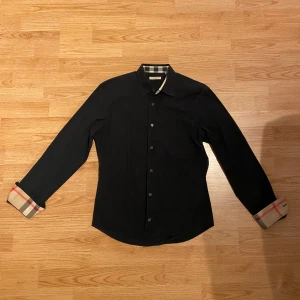 Burberry skjorta  - Svart burberry skjorta i väldigt bra skick utan fläckar eller andra liknande skador. Taggen innuti är bortklippt (se bild 5)  Size M, Tveka inte att kontakta vid minsta lilla fundering 🙏