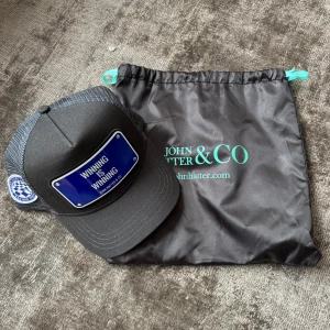 Oanvänd keps från John Hatter & Co - Snygg  keps från John Hatter & Co med blå skylt framtill där det står 'WINNING IS WINNING'. Kepsen har en logga på sidorna och justerbar passform. Perfekt accessoar för en cool och avslappnad stil.