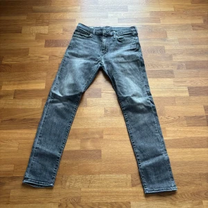 Grå raka jeans - Säljer ett par grå jeans med klassisk femficksdesign och raka ben. Jeansen har normal passform och stängs med dragkedja och knapp. Perfekta för en avslappnad stil.