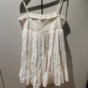 Vit somrig klänning med volang - Säljer en söt vit klänning med smock upptill och tunna axelband. 