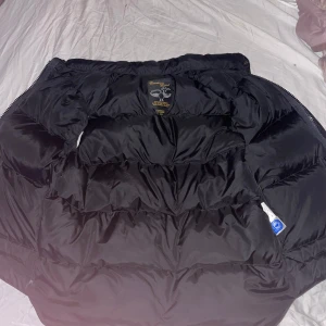 Svart dunväst från Canada Goose - Säljer en svart dunväst från Canada Goose i storlek M. Västen har hög krage, två stora framfickor och stängs med både dragkedja och knappar. Perfekt för lager-på-lager under kyliga dagar. Både tjej och kill väst.     Äkta!