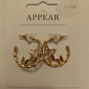Guldiga örhängen  - Säljer ett par guldiga örhängen från Appear med dekorativa fjärilar och glittrande stenar. Örhängena har en cirkelform och detaljer i både guld och silverfärg. Perfekt accessoar för att lyfta din stil. Supersnygga men kommer inte komma till användning. Helt Nya och aldrig använda!!! Nypris 59kr, mitt pris 25. Priset kan diskuteras 