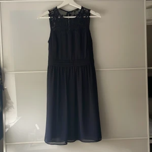 Svart ärmlös klänning med spetsdetaljer - Säljer en svart ärmlös klänning med fina spetsdetaljer upptill och rund halsringning. Från Vero Moda. Mycket bra skick. 