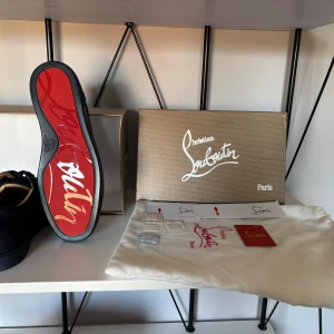 Mörkblå sneakers från Christian Louboutin - Säljer ett par exklusiva mörkblå sneakers från Christian Louboutin med klassisk röd sula och diskret leopardmönster i mocka. Skorna har snörning och rund tå, perfekt för dig som vill sticka ut med stil.