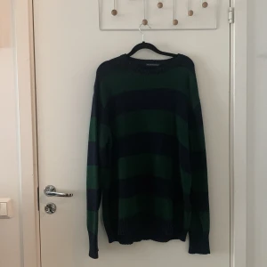 Randig stickad tröja från Brandy Melville - Mysig stickad tröja från Brandy Melville i grönt och mörkblått med breda ränder. Tröjan har lång ärm och avslappnad passform, perfekt för lager på lager. Klassisk rund halsringning och ribbade muddar.