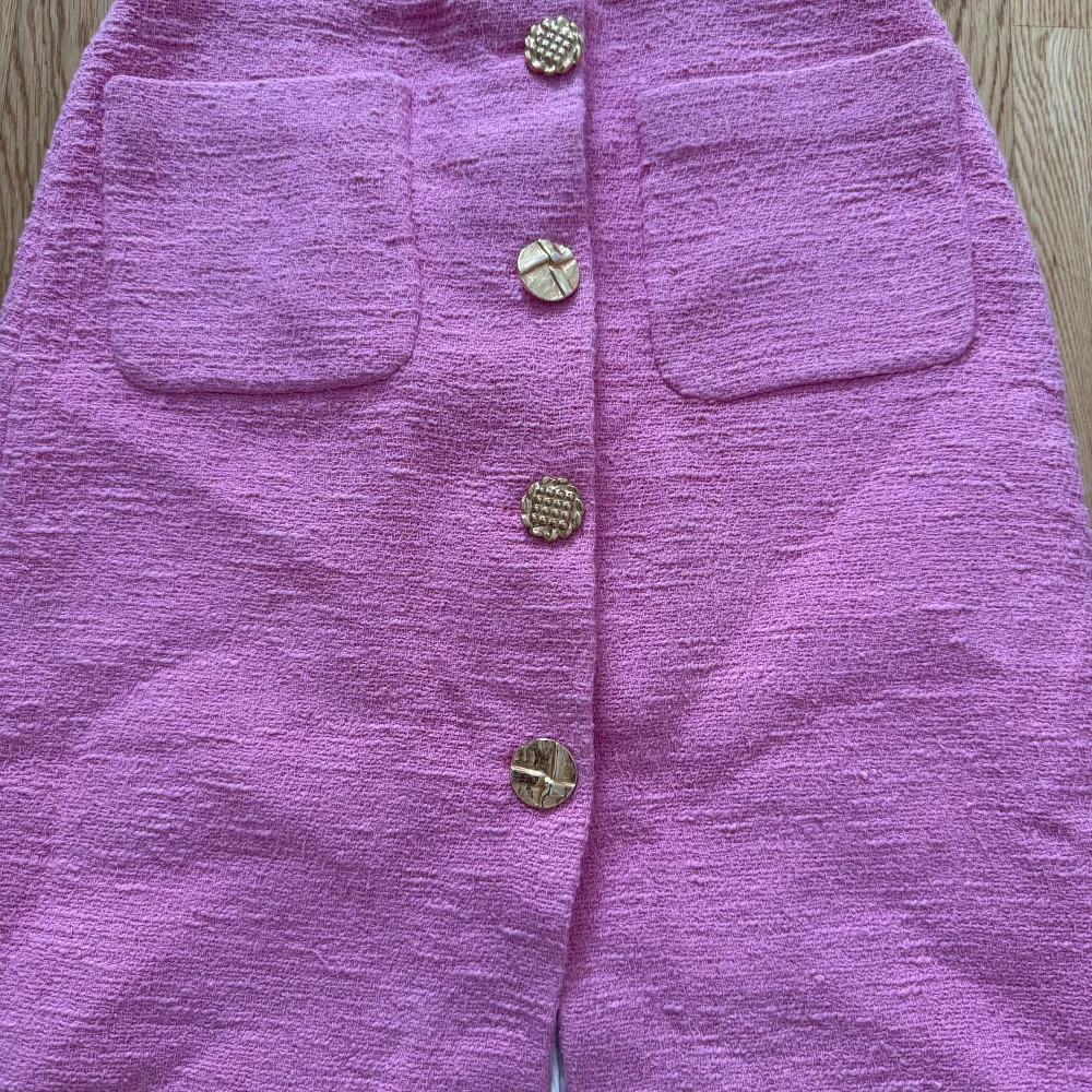 Säljer en snygg rosa långkjol med dekorativa guldknappar framtill och två stora fickor. Kjolen har en rak passform och en slits framtill för extra rörelsefrihet. Perfekt för dig som vill sticka ut med färg!. Hameet.