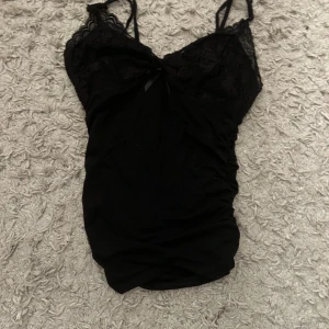 Svart spetslinne med smala axelband - Säljer ett svart linne med smala axelband och spetsdetaljer upptill. Linnet är från shein och är i storlek xs. Linnet är använt fåtal gånger och är i hyfsat bra skick. Linnet har en rosett framtill.❤️