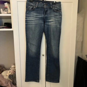 Blå jeansbyxor från ONLY - Säljer ett par klassiska blå jeansbyxor från ONLY med lätt slitna detaljer och raka ben. Byxorna har normal passform, fem fickor och stängs med dragkedja och knapp. Perfekta för en avslappnad stil.