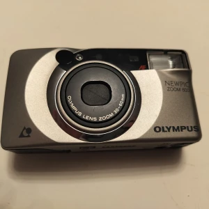 Y2K kamera  - Säljer en klassisk kompaktkamera från Olympus, modell Newpic Zoom 600. Kameran har en silverfärgad kropp och inbyggd blixt. Linsen har 30-60mm zoom och kameran är perfekt för dig som vill fånga Y2k estetiken 