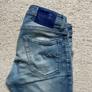 Jacob Cohen jeans Style 622 - Jacob Cohen Jeans – Style 622 Exklusiva ljusblå jeans från Jacob Cohen, modell Style 622. Normal passform, klassisk femficksdesign och knäppning med knappar i gylfen. Mjukt tvättat denim med diskreta slitningar och blå patch på linningen. Italienskt hantverk i toppklass – perfekt för dig som söker stil och kvalitet.
