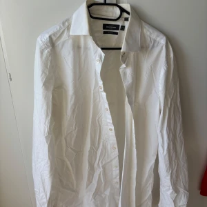 Vit skjorta från Dressmann - Klassisk vit skjorta från Dressmann i slim fit-modell. Skjortan har långa ärmar, knappar framtill och en stilren krage. Perfekt för dig som vill ha en enkel och stilren look. 