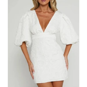 Vit Showpo klänning - Säljer en vit kort klänning med djup v-ringning och markerad midja. Klänningen har puffiga trekvartsärmar och en strukturerad yta som ger en lyxig känsla. Perfekt för sommarens tillfällen eller student! 🩷