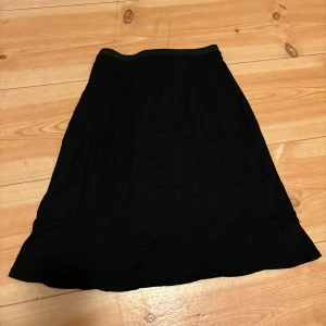 Svart kjol med dragkedja och knapp - En svart kjol med normal passform och resår i midjan. Kjolen har dragkedja och knapp i sidan för enkel på- och avtagning. Tidlös design som passar till många olika stilar. Mjuk och bekväm att bära.