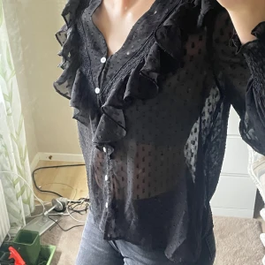 Svart blus med volanger  - Svart blus med fina detaljer och vita knappar fram, köpt från Plick och tror den är från SHEIN, står ingen storlek men skulle uppskatta att det är xs, s eftersom den är för liten för mig. Ingen defekter som jag upptäckt och verkar vara sparsamt använt på grund av dess fina skick💕💕💕pris kan diskuteras