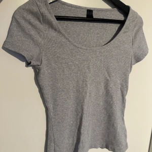 Grå ribbad t-shirt - En enkel och stilren grå ribbad t-shirt med rund halsringning och korta ärmar. Perfekt basplagg som passar till det mesta och är lätt att matcha med andra kläder.