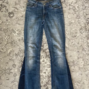 Blå bootcut jeans från Lee - Säljer ett par klassiska blå bootcut jeans från Lee med snygga utsvängda ben. Jeansen är tillverkade i bomull med lite stretch för extra komfort. Perfekta för dig som gillar retrostil och vill ha ett par jeans som sticker ut.