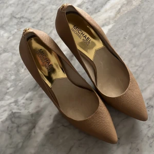 Beigea klackskor från Michael Kors - Snygga klackskor i beige från Michael Kors med spetsig tå och klack. Skorna har en elegant och stilren design med diskret gulddetalj vid hälen. Använd ett fåtal gånger och är i väldigt bra skick! ☺️