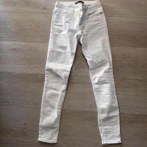 Vita skinny jeans - Säljer ett par vita skinny jeans med klassisk femficksdesign och knappgylf. Byxorna har en tight passform och är perfekta för en stilren look. Passar dig som gillar smala ben och enkel stil.
