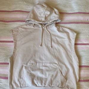 Beige ärmlös hoodie från H&M - Säljer en beige ärmlös hoodie från H&M i storlek L. Tröjan har huva med dragsko och en stor magficka framtill. Tillverkad i 100% bomull. Inga defekter eller skavanker!