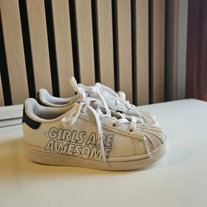  Super fina💞 Adidas Superstar 'Girls Are Awesome' sneakers. - Vita Adidas Superstar sneakers med svarta detaljer och texten 'GIRLS ARE AWESOME' på sidan. 💞Fraktkostnaden beror på adressen💞💞