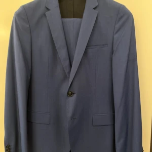 Blå Hugo Boss kavaj - Snygg blå kavaj och kostymbyxor från Hugo Boss, tillverkad i en exklusiv ull- och silkesblandning från Lanificio di Tollegno. Klassisk modell med smal passform, enkla knappar och fickor framtill. Perfekt för bal eller fest!☺️