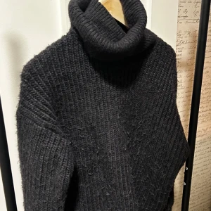 Svart stickad polotröja från H&M - Mysig svart stickad polotröja från H&M. Tröjan har en hög polokrage och är grovstickad med lång ärm. Perfekt för kyliga dagar och enkel att matcha med olika outfits.