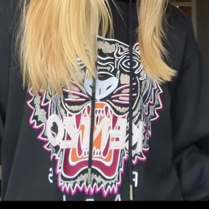 Svart hoodie från Kenzo - Säljer en svart hoodie från Kenzo med ett stort tigertryck och texten 'Kenzo Paris' på framsidan. Hoodien har en justerbar huva med dragsko och ribbade muddar vid ärmslut och nederkant. Perfekt för en cool och avslappnad stil. Aldrig använd och lappen är kvar, pris kan diskuteras 💗💗Köpte för 3500kr