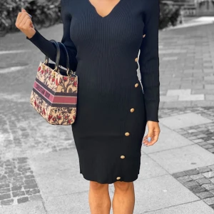 Svart ribbad klänning med guldknappar - Snygg svart ribbad klänning med lång ärm och v-ringning. Klänningen har en tight passform och dekorativa guldknappar längs sidan som ger en extra touch. Perfekt för dig som gillar stilrena och trendiga plagg.