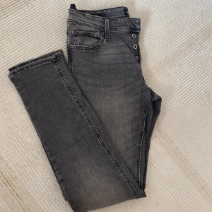 Grå slim jeans från Jack & Jones - Snygga grå jeans från Jack & Jones i modellen Slim Glenn. Jeansen har en slim passform, klassisk och knäppning med flera knappar. Materialet är stretchigt jeans för extra komfort. Perfekta till en avslappnad streetstil.